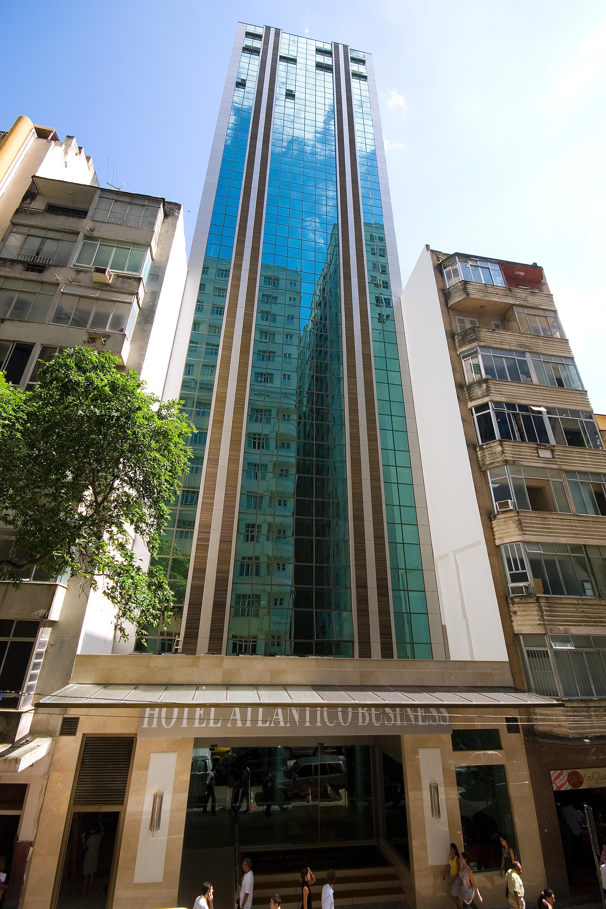 Hotel Atlantico Business Centro Rio de Janeiro Luaran gambar The photo shows a modern multi-story building with a sleek glass facade. The building appears to have several floors with large windows, reflecting sunlight, and is flanked by a tree on one side and an older, more traditional residential structure on