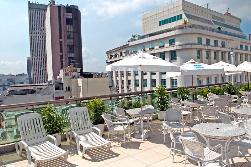 Hotel Atlantico Business Centro Rio de Janeiro Luaran gambar The photo shows a rooftop area with several white lounge chairs and circular tables. There are umbrellas providing shade over some of the seating. In the background, there are tall buildings, including a modern skyscraper with a distinct architectura